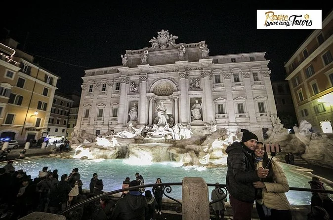 The Trevi Fountain floodlit at night with visitors standing in the square