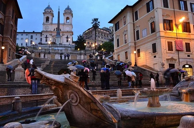 The Spanish Steps and the Barcaccia fountain at dusk with people walking in the square