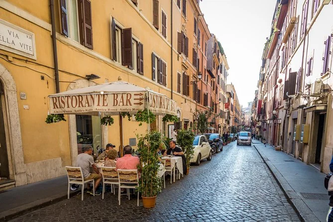 A cobbled Roman street lined with ochre buildings and a café
